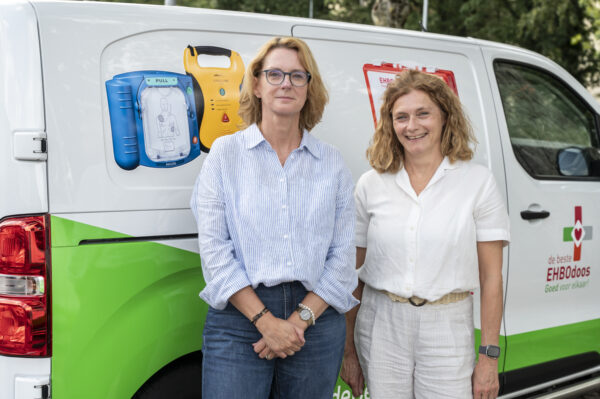 Nancy en Irene van de backoffice poseren voor de bedrijfsbus van deBesteEHBOdoos.